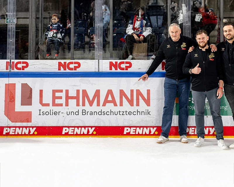 Foto von Tobias und Andreas Lehmann auf dem Eis der Ice Tigers Nürnberg, sie zeigen auf ihre Bandenwerbung.